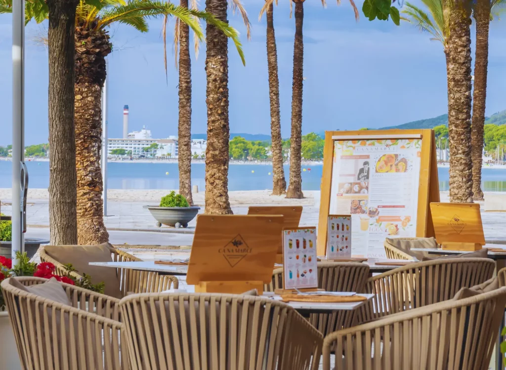 Terraza del restaurante Ca Na Marcè frente al puerto de Alcudia, Mallorca, con mesas preparadas para disfrutar de brunch y cocina mediterránea