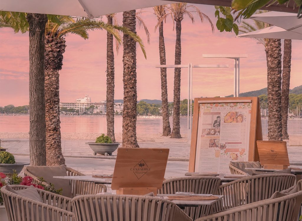 Terraza del restaurante Ca Na Marcè frente al puerto de Alcudia, Mallorca, con mesas preparadas para disfrutar de brunch y cocina mediterránea